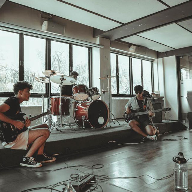 A band performs in a music studio, surrounded by instruments and sound equipment, creating a lively atmosphere.